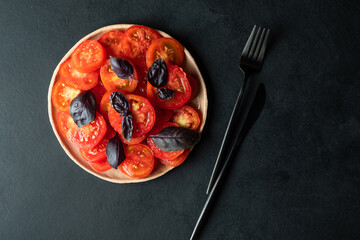 Tomatoes chopped with circles, with a basil on a round plate on a dark background. 