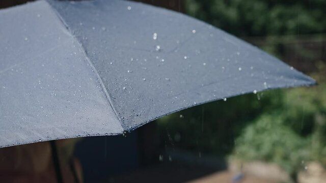 Summer rain on a sunny day. Drops of water flow down from the surface of the gray umbrella.