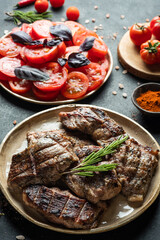 Pieces of grilled carp on a round plate, tomatoes, peppers, spices on a dark background. 