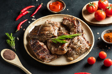Pieces of grilled carp on a round plate, tomatoes, peppers, spices on a dark background. 