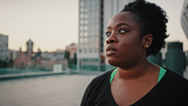 Young overweight african american lady standing outdoors in urban center and looking aside, feeling tired and exhausted