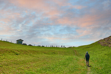 Fototapeta premium Middle-aged woman with straw hat and backpack, walking along path in Suances at dawn