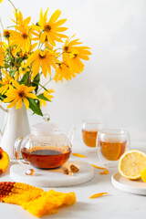 Cozy autumn. Fall composition, yellow flowers bouquet, hot teapot, two cups of tea and a warm scarf on white table background. Tea party. Poster, greeting card. Copy space