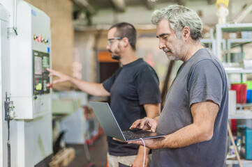 Two field service maintenance engineer technician electrician inspect and control machine hardware and software system with laptop computer. Electric installation