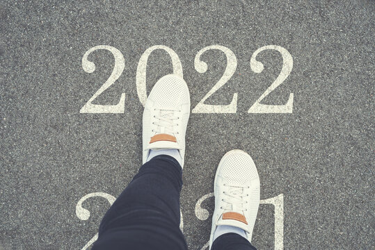 Happy New Year 2022. Women's legs cross 2021 and step 2022. Top view of white sneakers on asphalt road with text 2022