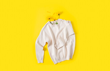 Autumn shopping, discount and sale concept. Knitted sweater and autumn flowers on a bright yellow background. Flat lay, copy space. Fall promotion. Clothes care, dry cleaning, ecological production