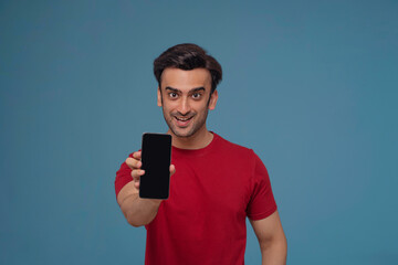 Portrait of a young man showing mobile phone in his hand against plain background.