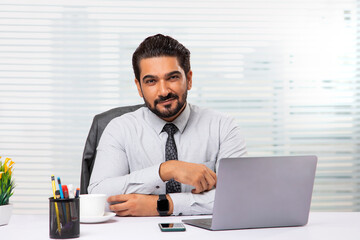 An employee sitting in his office looking at camera,smiling.