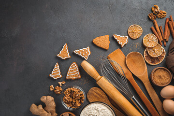 Ginger cookies, ingredients and kitchen utensils on a dark background. Top view. Christmas background.