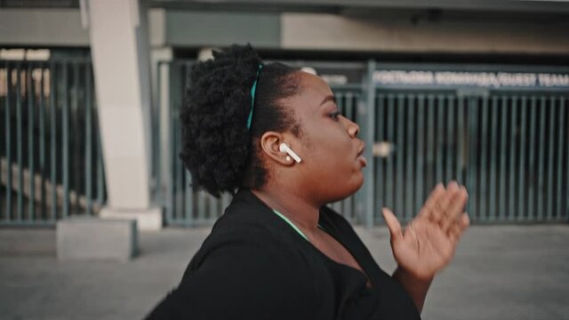 Young overweight african american woman practicing cardio training, running alone in urban area, tracking shot