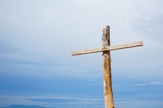 A cross sign made by old wood is at the right side of photo. White and blue sky in the background.  A religious symbol, crucifix, death and spiritual themes.