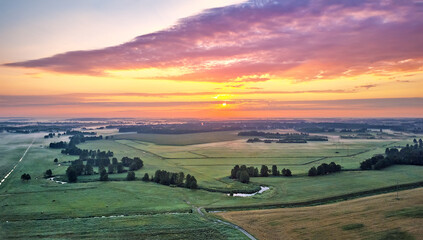 Dramatic summer sunrise. Panorama misty landscape. Foggy Morning on river aerial view. Green fields...