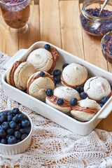 Almond cookies with chocolate cream. Blueberries, cornflower blue tea, wood background, side view.