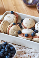 Almond cookies with chocolate cream. Blueberries, cornflower blue tea, wood background, side view.