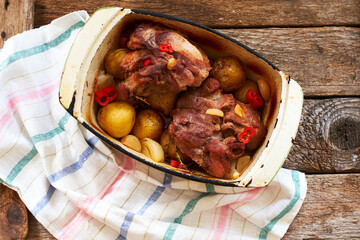 Baked meat with vegetables in a cauldron. Side view, wooden background.