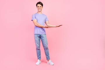 Full length body size view of attractive cheerful guy demonstrating copy space ad isolated over pink pastel color background