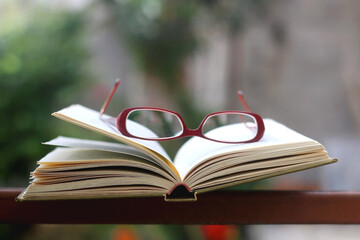 Vintage hardcover book and red reading glasses in a garden. Selective focus.