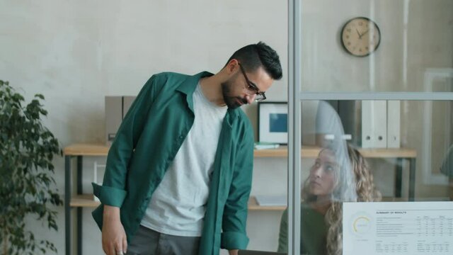 Middle eastern businessman walking in office, speaking with Caucasian woman and then helping Afro-American male colleague with disability in wheelchair during workday