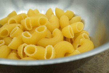 Raw elbow Macaroni (Gomiti Pasta) in stainless steel bowl on wooden table, Close up