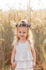 Little cute smiling girl with a wreath of flowers on her head in the summer in nature