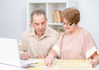 Senior couple planning holiday use map and laptop