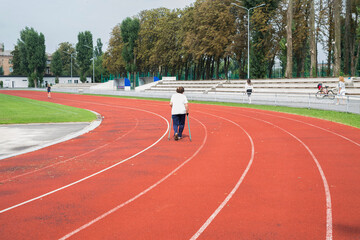 An elderly woman is engaged in walking with sticks in the stadium.