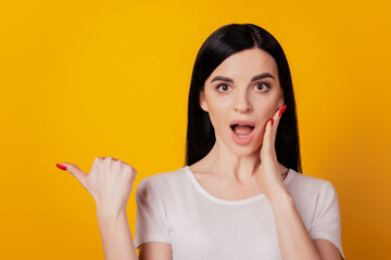 Portrait of excited young girl point thumb empty space advert choice amazed sale isolated over yellow color background