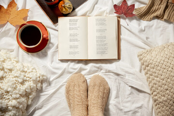 season and leisure concept - book, cup of coffee, feet in warm socks and autumn leaves in bed