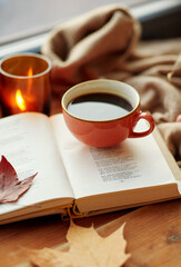 season, leisure and objects concept - cup of coffee, book, autumn leaves and candle on window sill at home