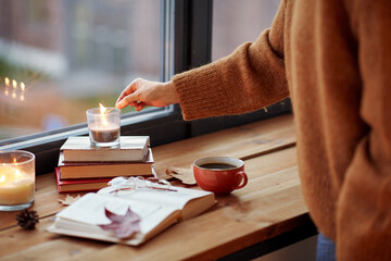 holidays and leisure concept - woman's hand with match lighting candle at home on halloween