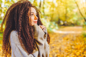 Beautiful afro-haired woman wearing warm sweater walk in autumn park at sunny warm day. Portrait of woman outdoor.