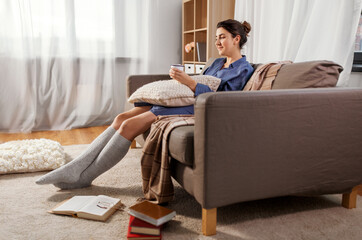 people and leisure concept - young woman with books on floor drinking hot chocolate with marshmallow sitting on sofa at home