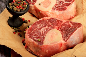 Raw Beef Shin with bone on backed paper decorated with spices. Old wooden board background 