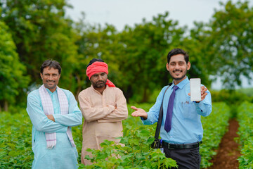 Young indian agronomist or banker showing tablet with farmers at agriculture field.
