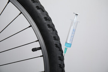 Bike wheel with syringe on light background, closeup. Using doping in cycling sport concept