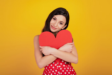 Portrait of lovely lady embrace big heart card wear dotted red dress on yellow background