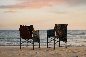 Fototapeta na wymiar Camping chairs and backpack on sandy beach near sea