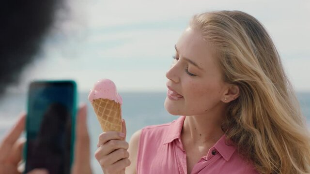 beautiful blonde woman with afro eating ice cream on beach posing for friend taking photo using smartphone girl friends sharing fun summer day on social media 4k