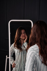 A pretty woman stands in her pajamas and looks in the mirror.