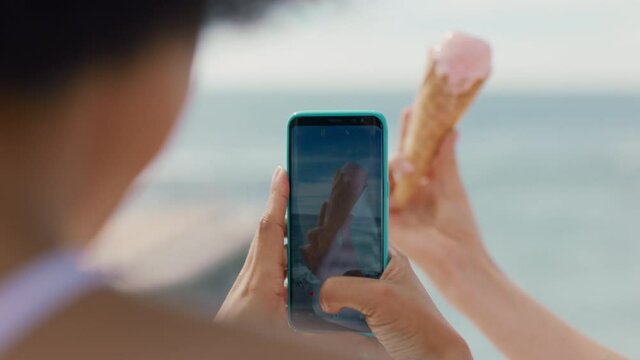 young woman holding ice cream on beach with friend taking photo using smartphone sharing delicious dessert on social media 4k