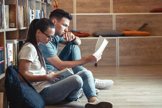 Two students reading a book by the book shelf at the university campus library.