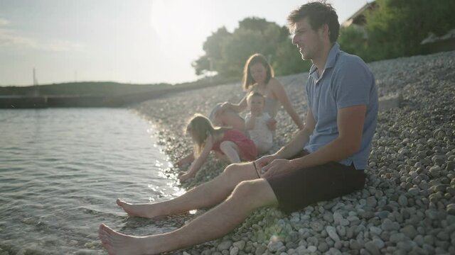 Slow motion - Young family sitting on the beach and throwing rocks into the sea 