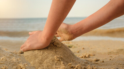 hands of a child play with sand on the beach