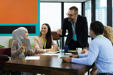 Asian Muslim business woman in hijab headscarf sitting on wheelchair presenting of her work to corporate colleagues in meeting in the modern office. diverse corporate colleagues and multicultural