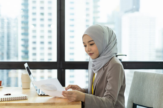 Asian Muslim business woman in hijab headscarf working with with paper chart in the modern office. business people, diversity and office concept