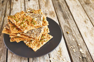 Stack of crunchy crispbread on black plate on wooden table. Whole Grain crisp bread with pumpkin, sunflower, chia, linen and sesame seeds. Healthy snack. Bio-organic dieting product.