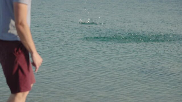 Slow motion, close up - Young adult caucasian man skipping stone on water