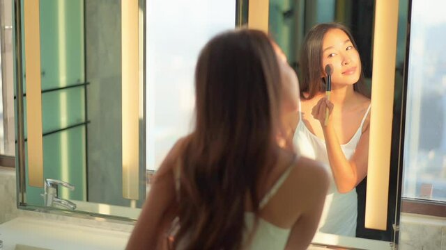 A beautiful young woman with flawless skin applies makeup with a blush brush.