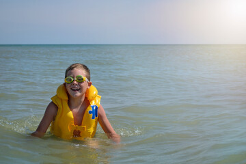 boy in a life jacket in the water. joyful child spends summer vacation at the sea on a sunny day.