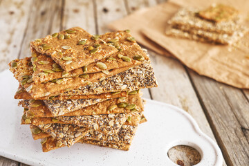 Crunchy crispbread on white ceramic cut board on wooden table. Whole Grain crisp bread with pumpkin, sunflower, chia, linen and sesame seeds. Healthy snack. Bio-organic dieting product.